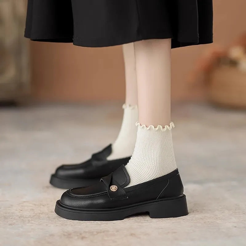 Black penny loafers with gold detail and platform sole, styled with ruffled socks.