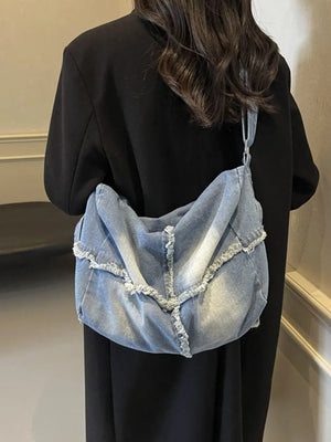 Light wash denim crossbody bag with frayed edges and slouchy silhouette.