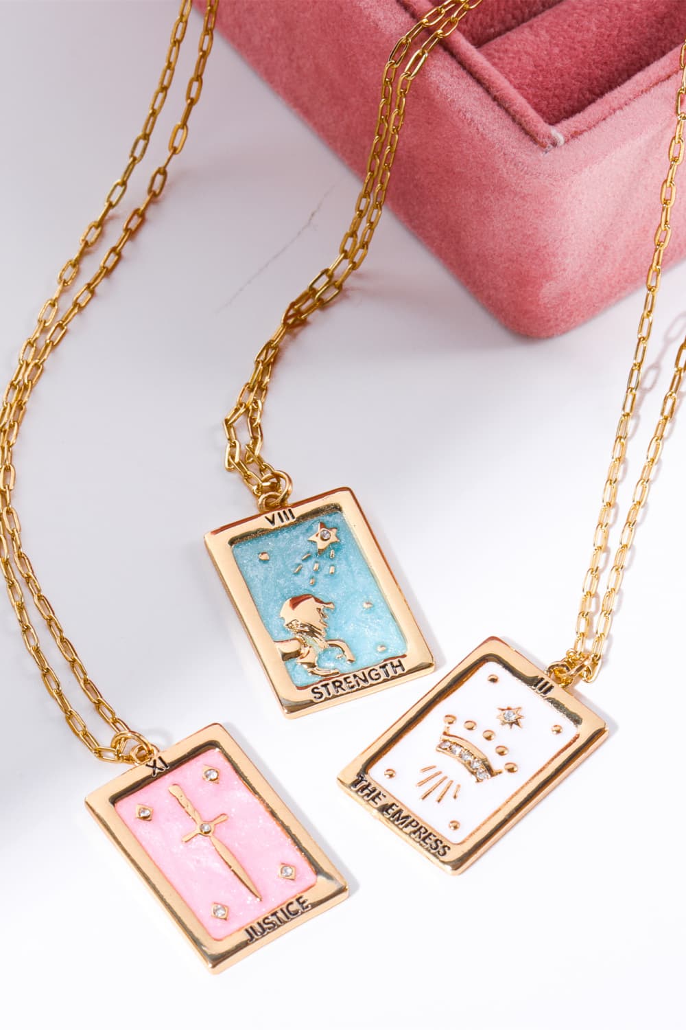 Tarot card pendant necklaces in light blue, white, and blush pink with gold chains and charms.