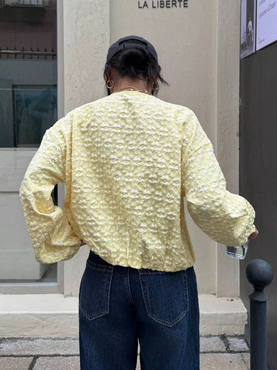Yellow bomber jacket with textured floral embossed pattern and zip closure.