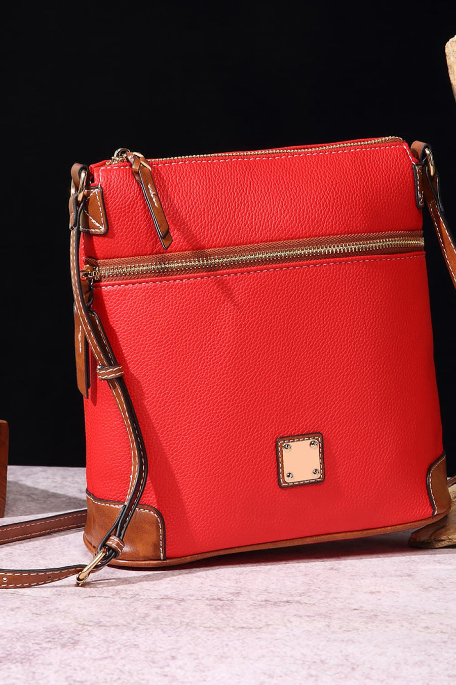 Red leather crossbody bag with brown trim and brass hardware.