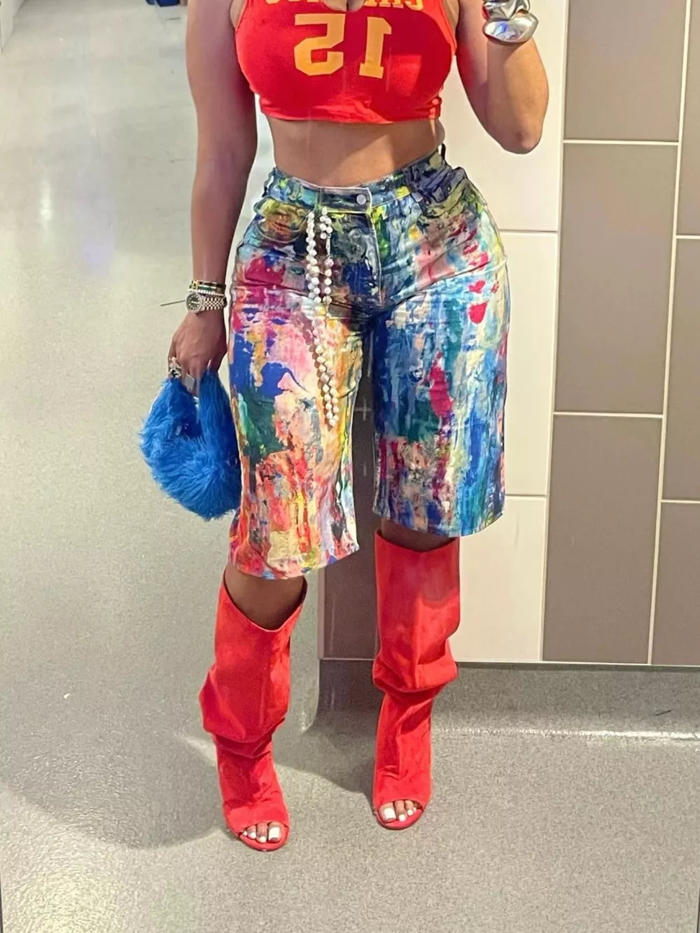 Denim shorts with abstract paint splatter pattern, pearl belt, red crop top, and red slouch boots.