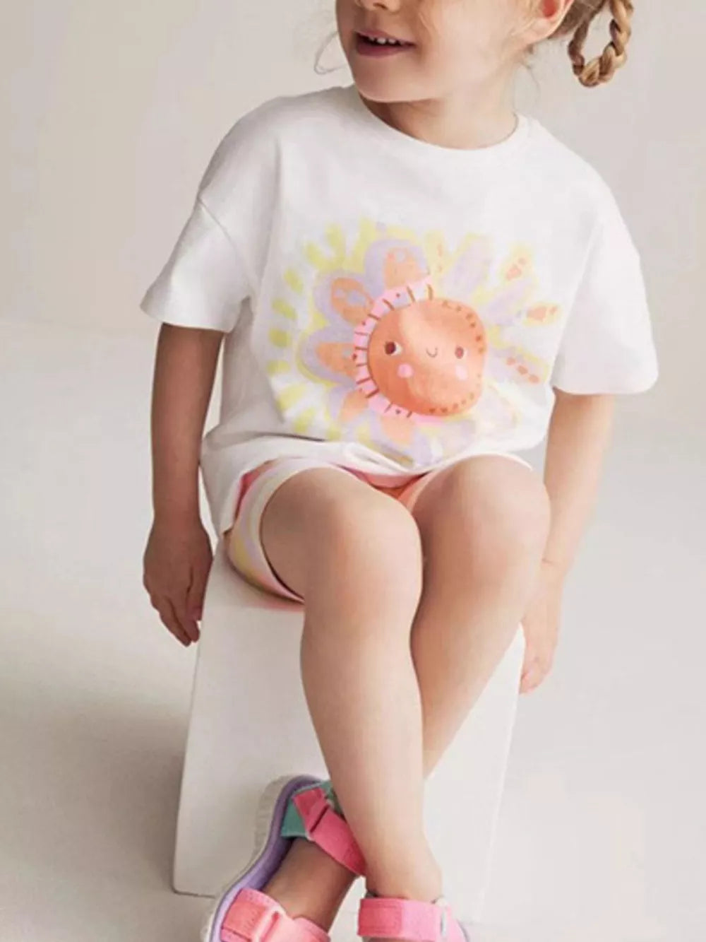 White cotton t-shirt with a playful cartoon sun graphic, short sleeves, and a crew neck.