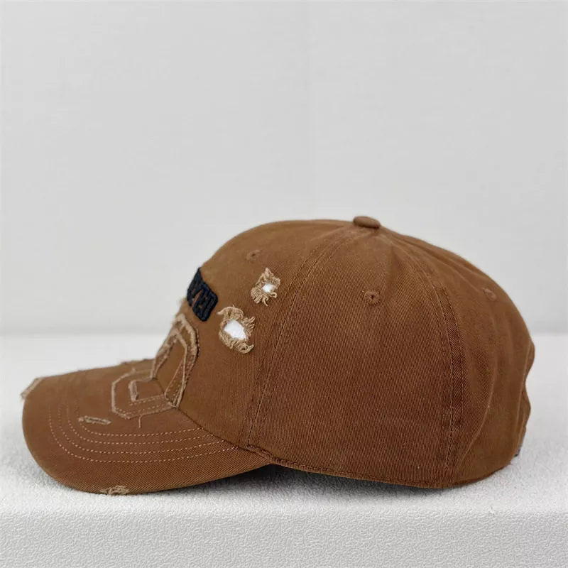 Brown distressed baseball cap with embroidered patches and frayed details.