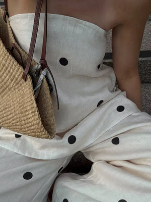 White linen strapless jumpsuit with black polka dots and a straw bag