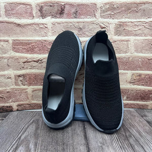 Black breathable round toe slip-on sneakers with a knit upper and grey sole.
