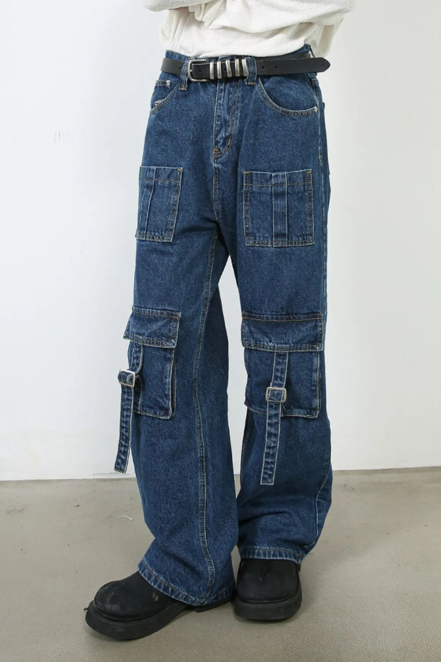 Medium wash denim cargo pants with buckle strap pockets and wide leg cut.