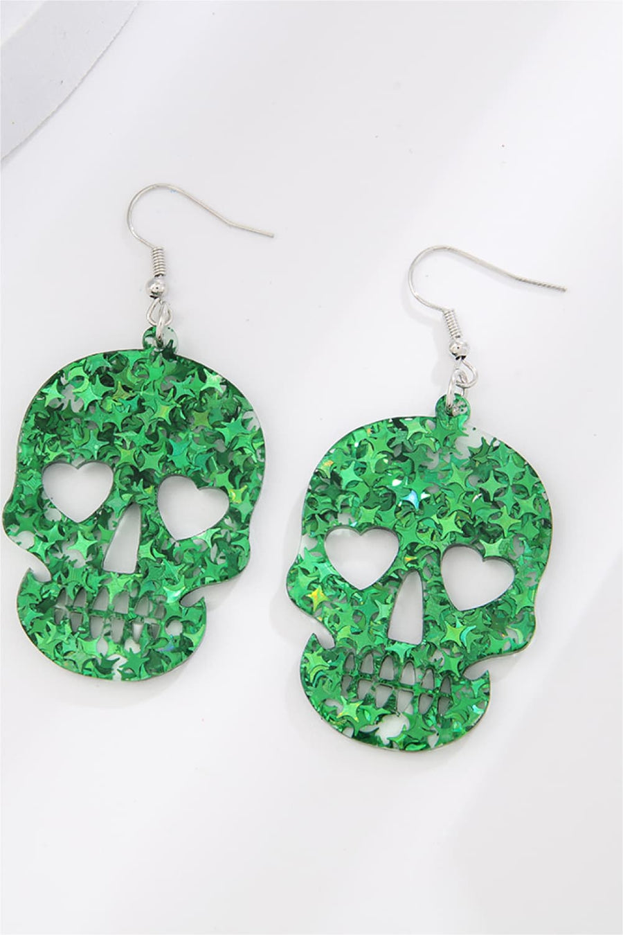 Green glitter skull earrings with heart eye cutouts and starburst pattern.