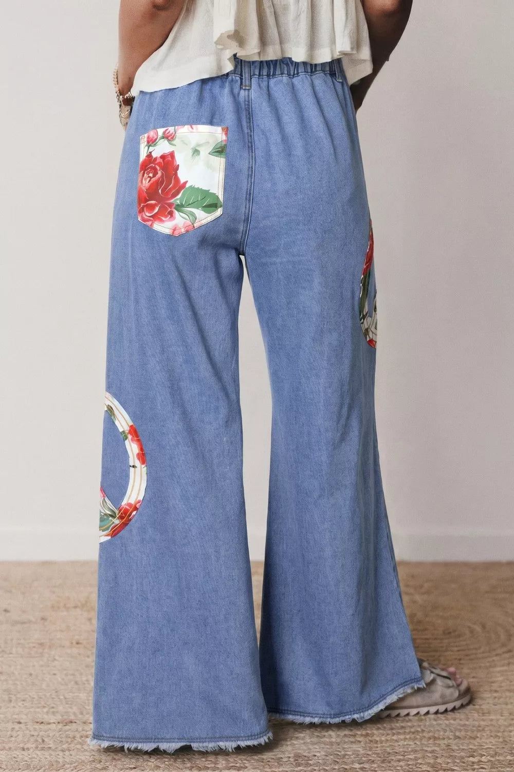 Floral appliqué wide-leg jeans in light wash denim with a peace sign detail and rose pocket.