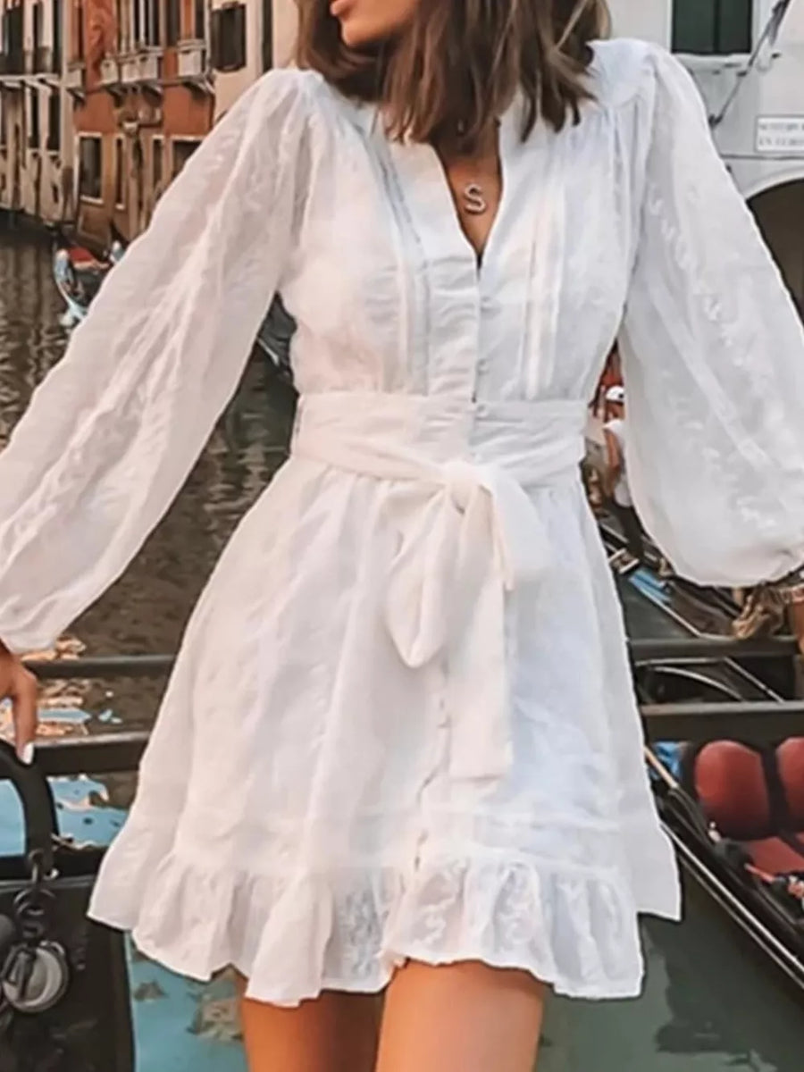 White textured mini dress with puff sleeves, V-neck, button front, tie waist, and ruffled hem.