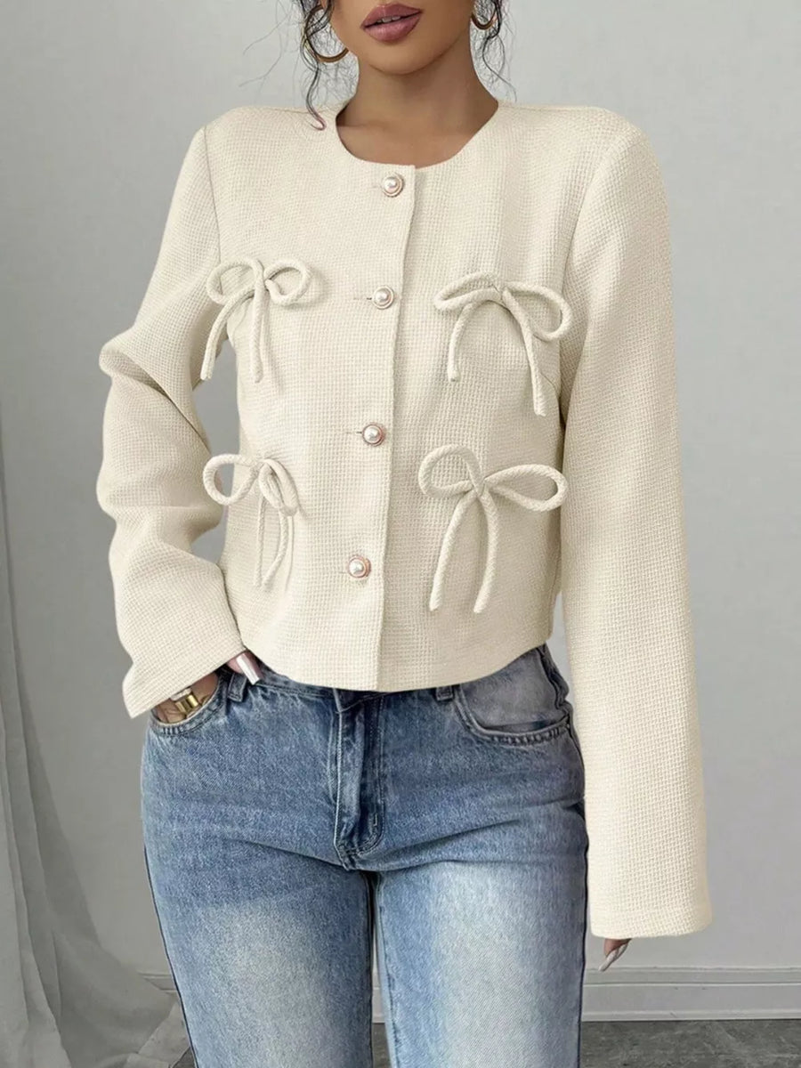 Cream textured jacket with bow details and pearl buttons, crew neck, long sleeves.