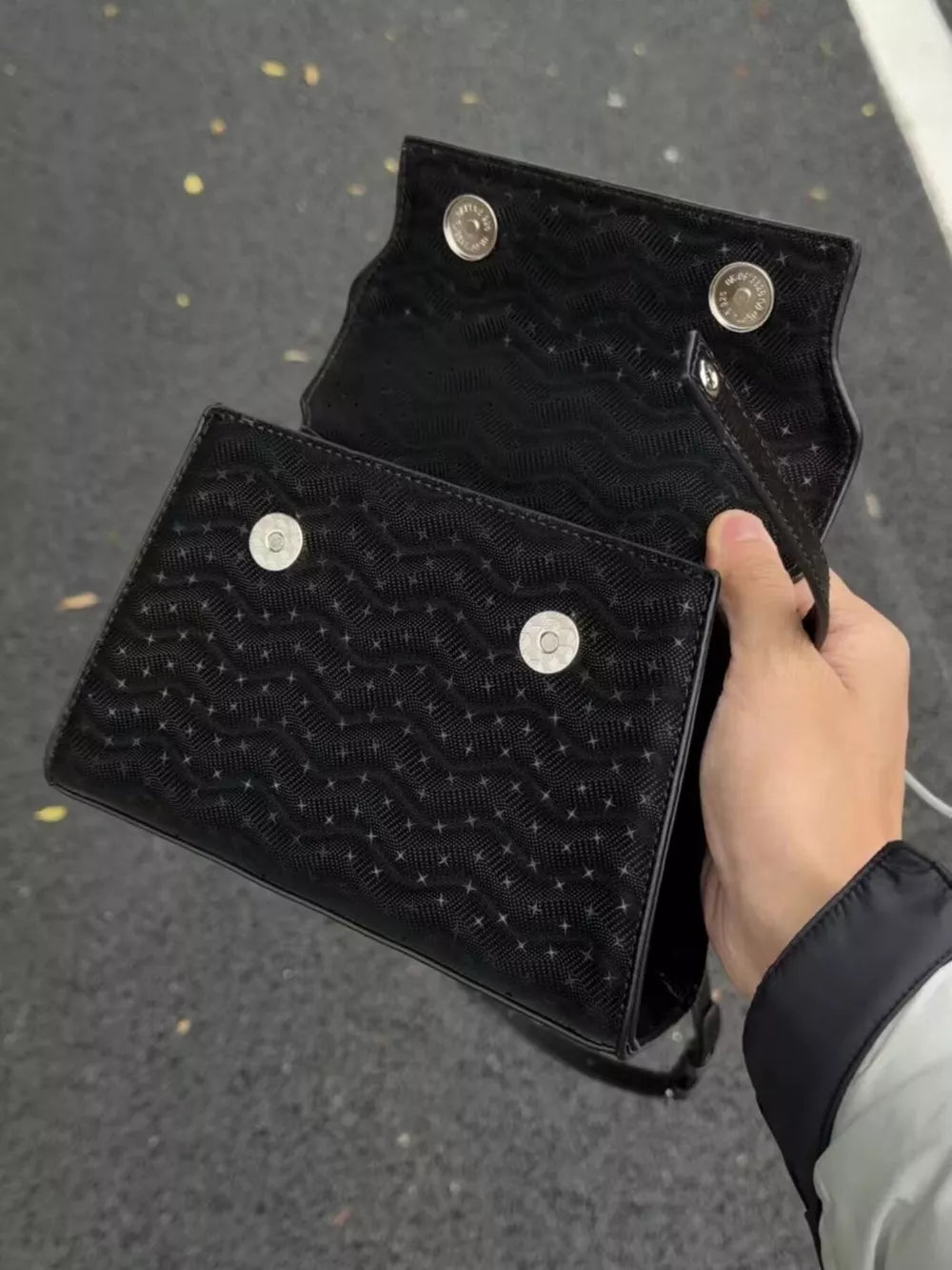 Chic black embossed mini handbag with snap closure and charm detail.