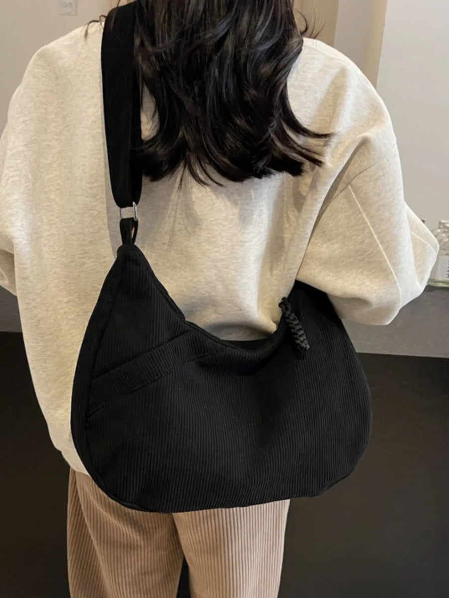 Black corduroy crescent shoulder bag with braided detail and adjustable strap.