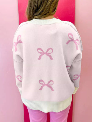 Beige drop shoulder sweater with all-over pink bow print, crew neck, and ribbed hem.