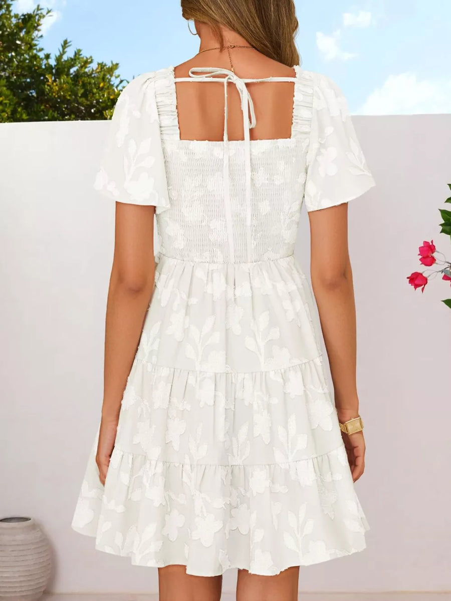 White smocked mini dress with tiered skirt, puff sleeves, and square neckline with tie back.
