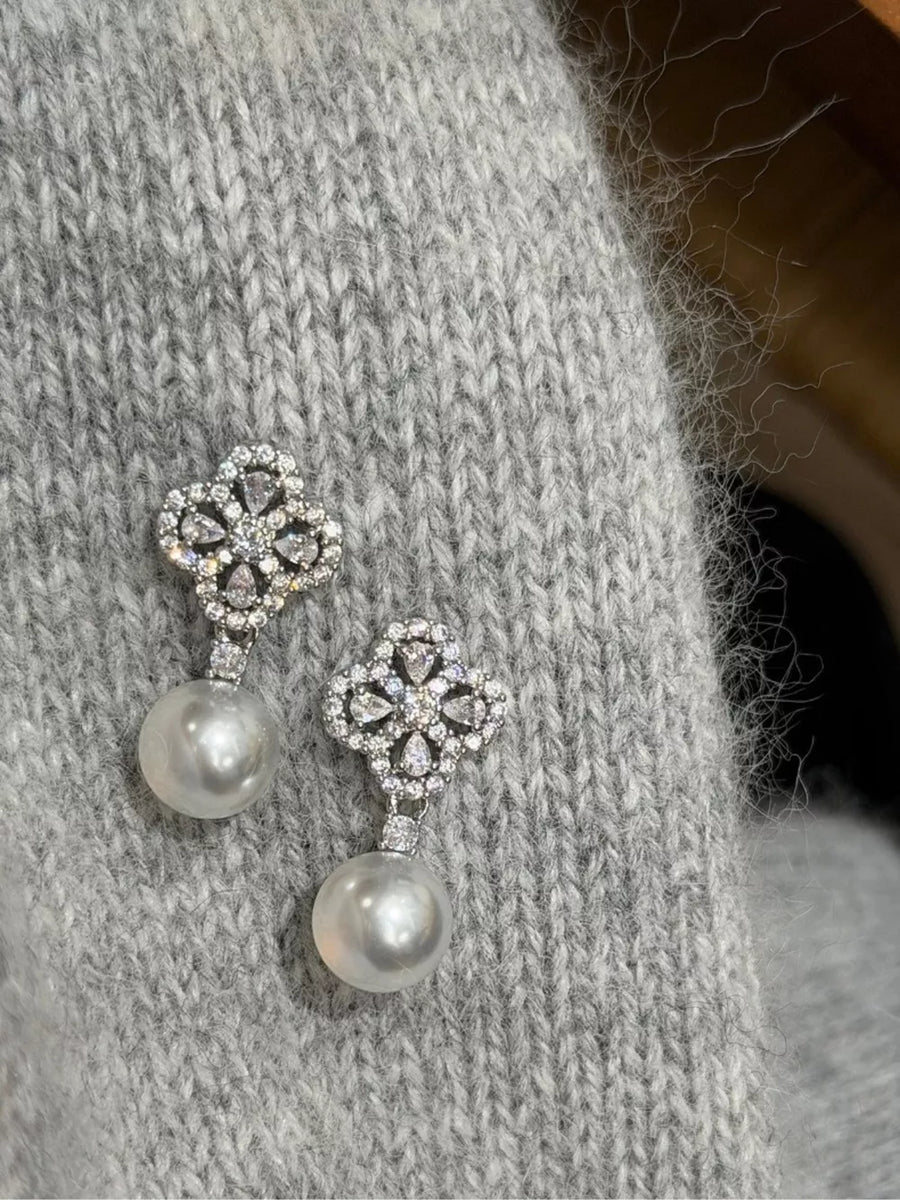 Elegant clover zircon and pearl drop earrings with a beige sweater detail.