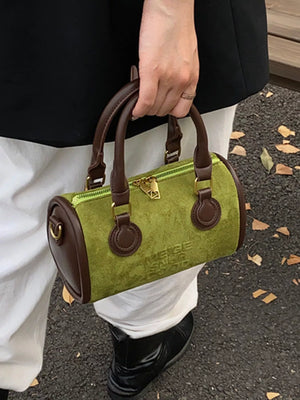 Small barrel crossbody bag in green suede with brown leather trim and handles.