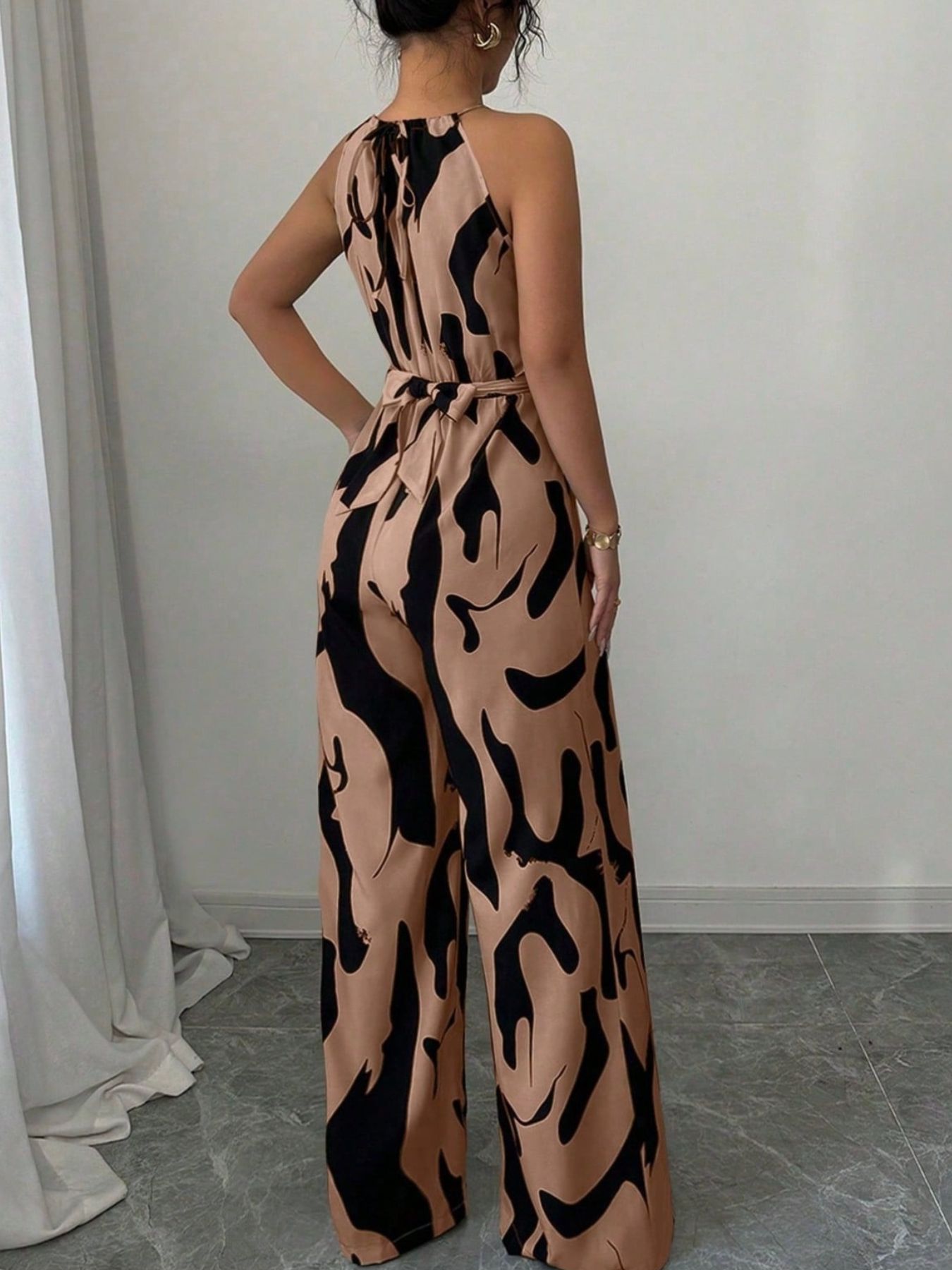 Elegant wide-leg jumpsuit in tan with abstract black print, halter neck, and tie waist.