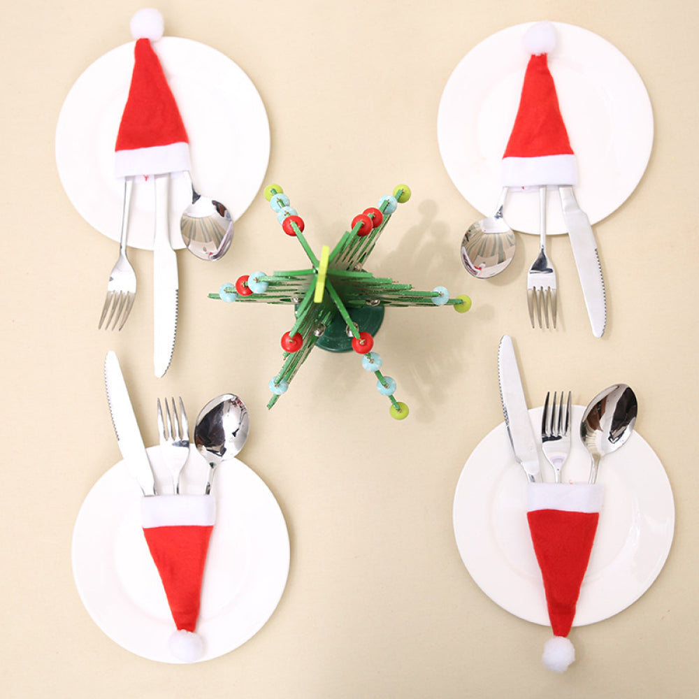 Red Santa hat cutlery holders on plates with silverware, plus a festive green tree centerpiece.