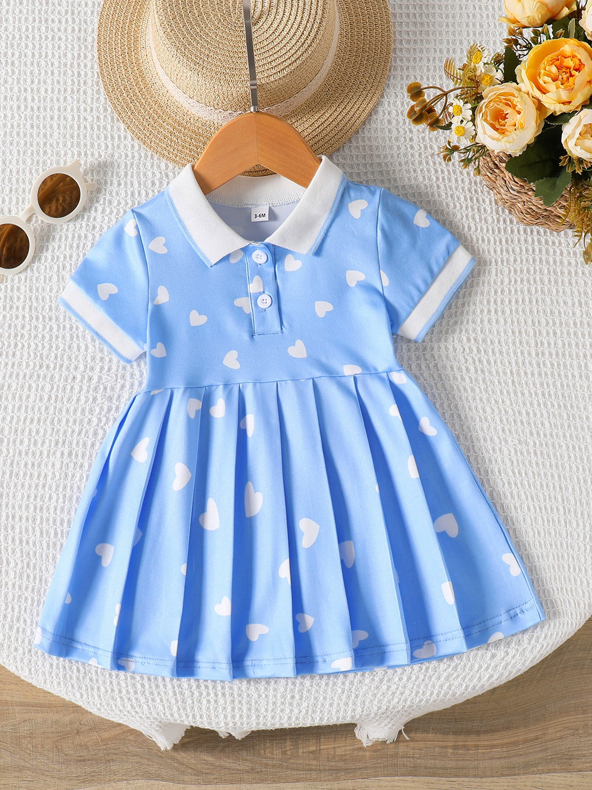 Baby dress with white hearts on blue, white collar, short sleeves, and pleated skirt.