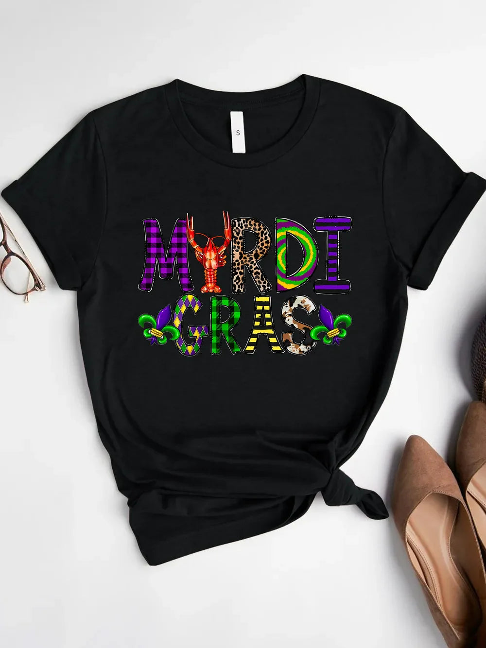 Black Mardi Gras graphic tee with mixed texture letters and fleur-de-lis accents.