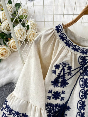 Cream tie-neck blouse with intricate blue embroidery and balloon sleeves.