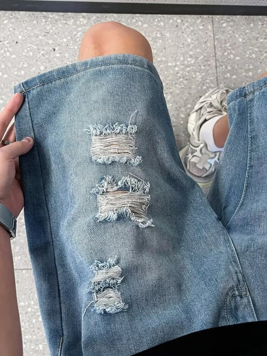 Men's light wash denim shorts with distressed rips and wide leg cut.