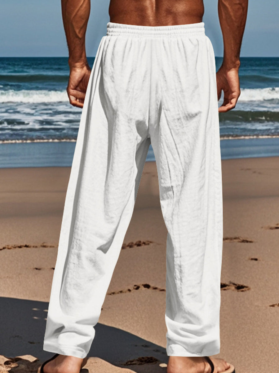White relaxed fit drawstring sweatpants with button-fly, cotton blend, on a man at the beach.