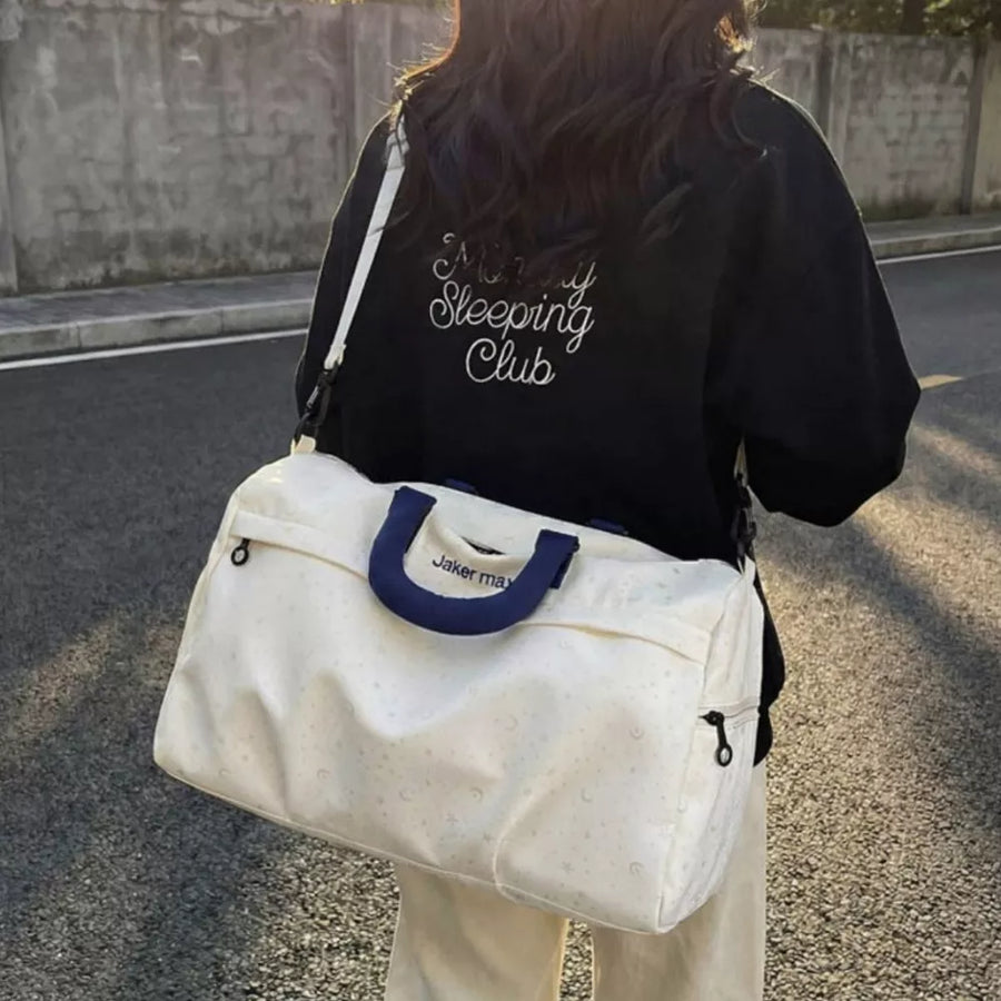 Cream white duffel bag with crescent moon pattern and navy handles, adjustable strap.