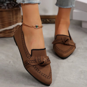 Brown chain-stitched knit bow pointed flats with black trim and an evil eye anklet.