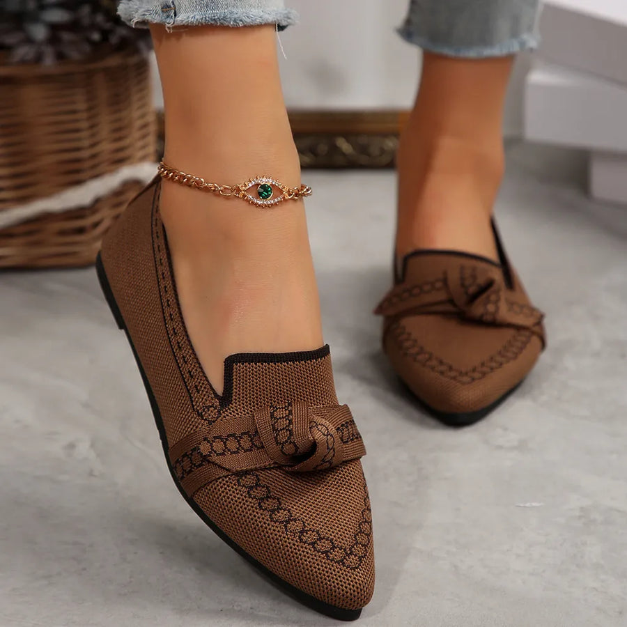 Brown chain-stitched knit bow pointed flats with black trim and an evil eye anklet.