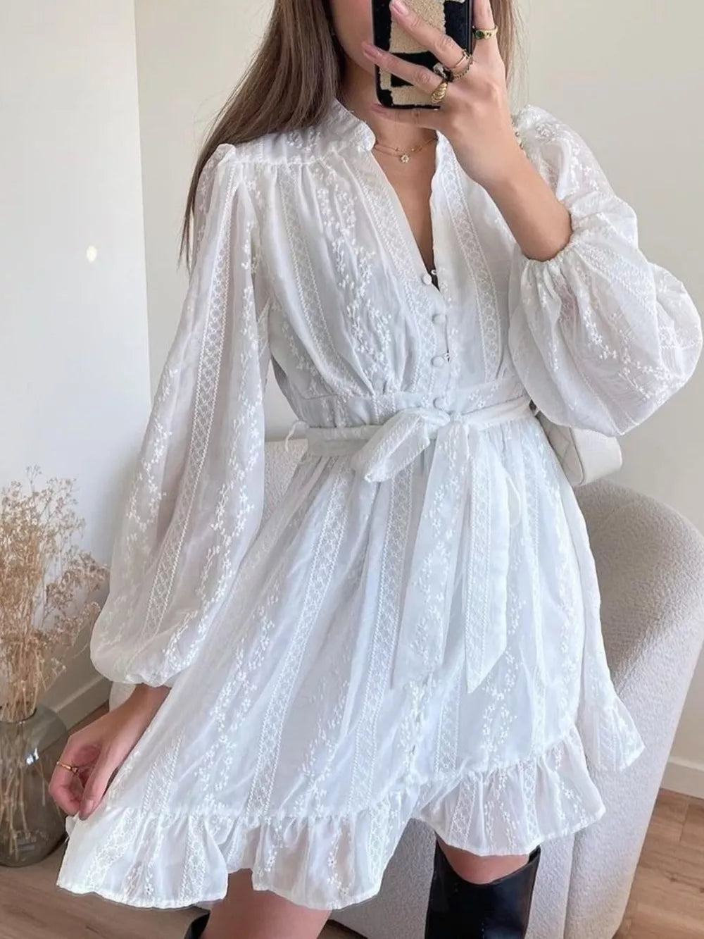 White eyelet mini dress with V-neck, balloon sleeves, tie waist, and ruffled hem
