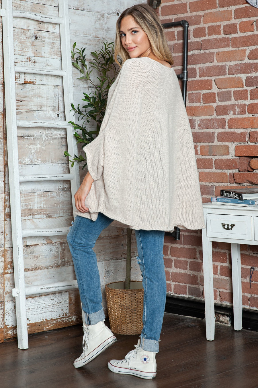 Cream knit sweater with relaxed fit and cape sleeves, styled with jeans.