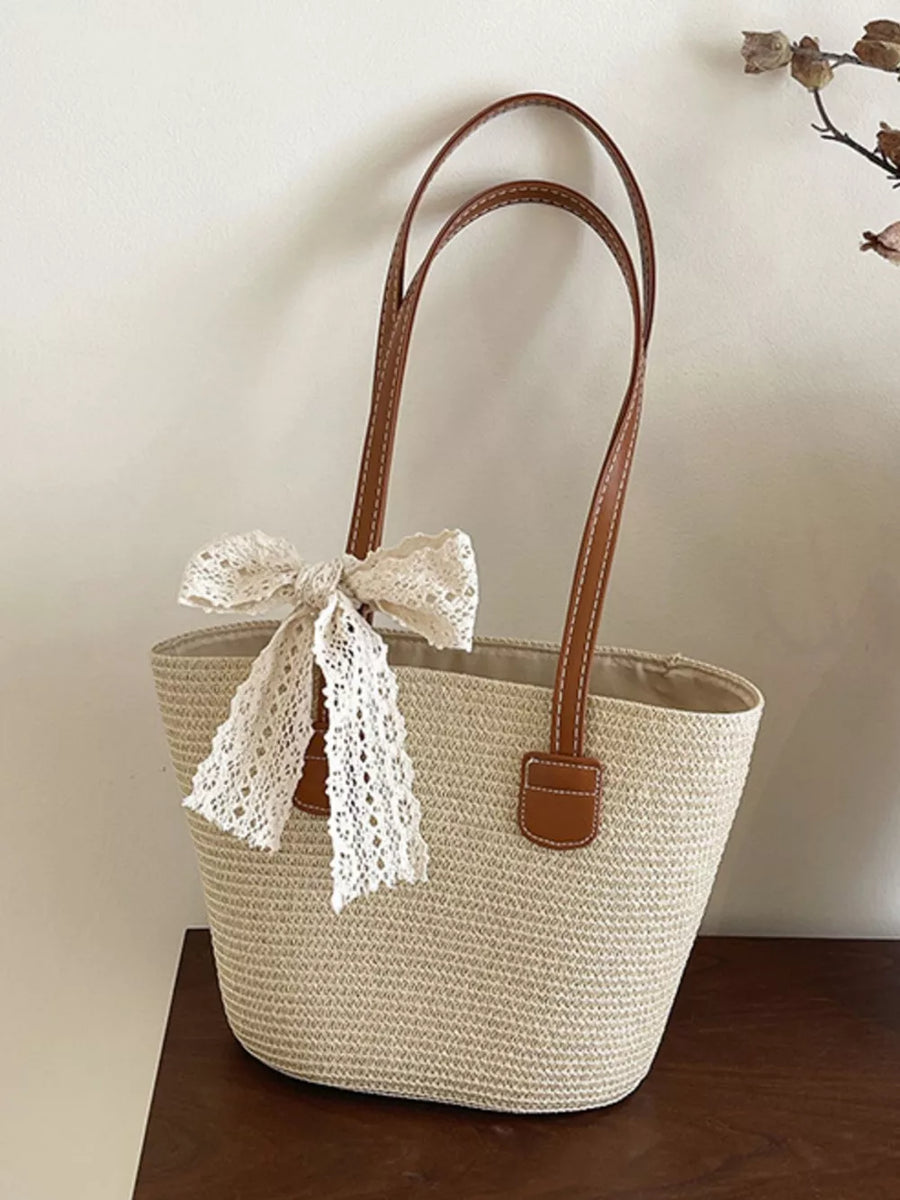 Charming straw shoulder bag in off-white with lace bow detail and brown leather straps.