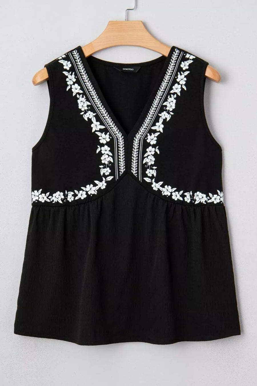 Black sleeveless V-neck top with white floral embroidery and textured fabric.