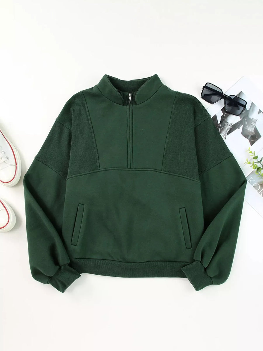 Dark green half zip stand collar sweatshirt with textured panels and front pockets.