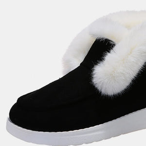 Black suede slip-on booties with white shearling trim and white sole.