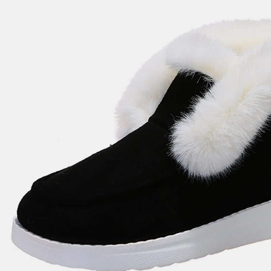 Black suede slip-on booties with white shearling trim and white sole.