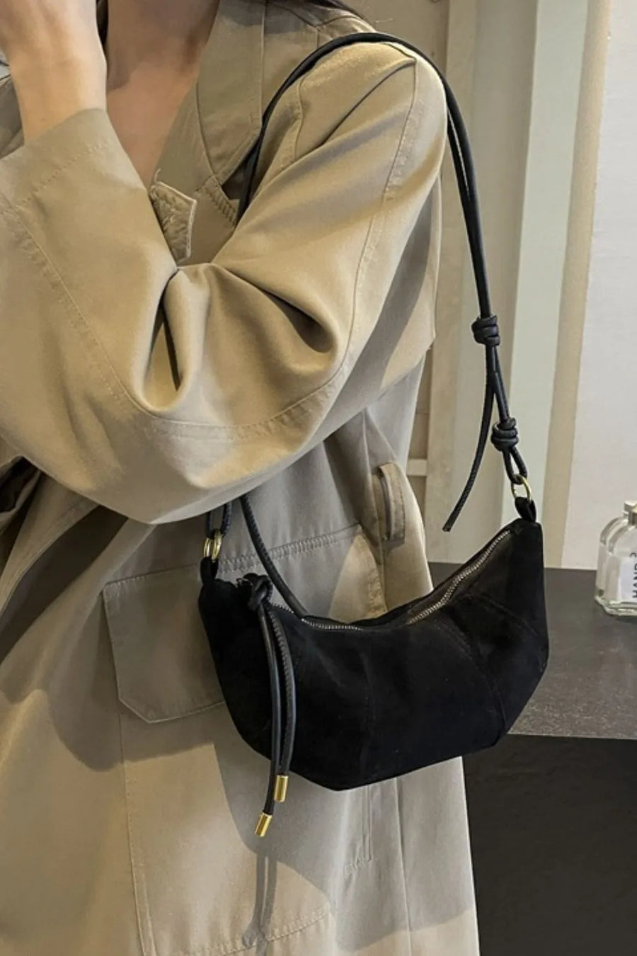 Black suede crescent shoulder bag with knot detail and gold hardware.