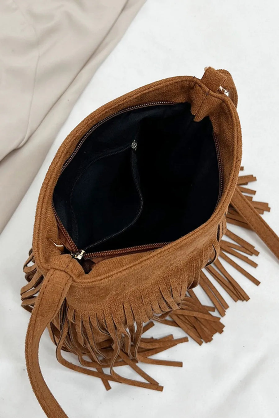 Brown suede crossbody bag with fringe detail and zippered main compartment.