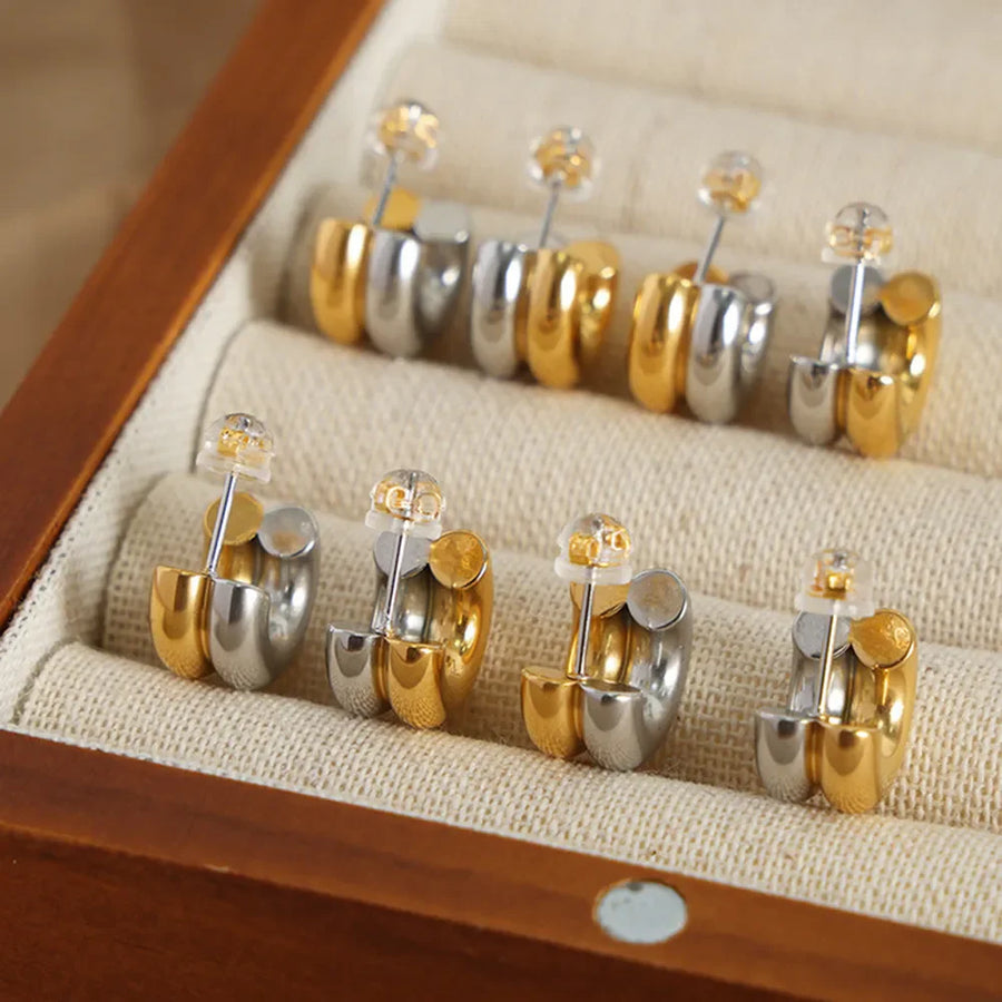 Dual-tone sculptural C-hoop earrings in gold and silver, shown in a jewelry box.