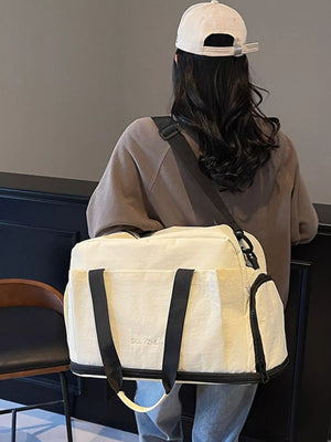 Off-white Oxford cloth travel tote bag with black trim and handles, featuring a zippered side pocket.