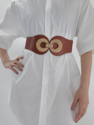 Caramel elastic belt with gold textured double ring buckle cinching a white dress.