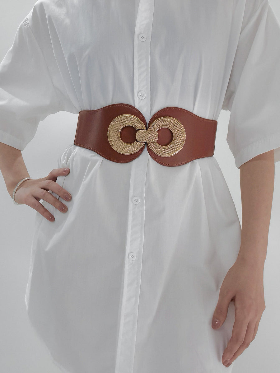 Caramel elastic belt with gold textured double ring buckle cinching a white dress.