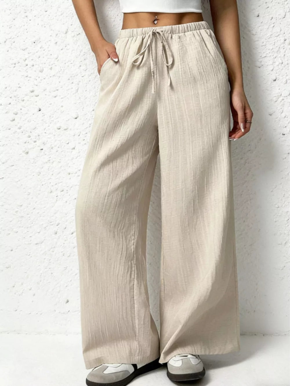 Beige cotton wide-leg pants with adjustable drawstring and pockets, styled casually.