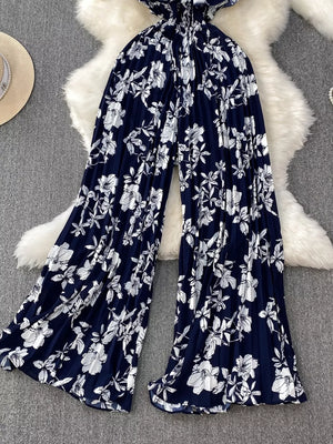 Dark blue floral pleated wide-leg romper with smocked waist and flowy legs.
