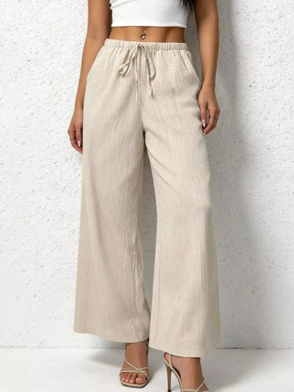 Relaxed beige cotton wide-leg pants with adjustable drawstring waist and pockets.