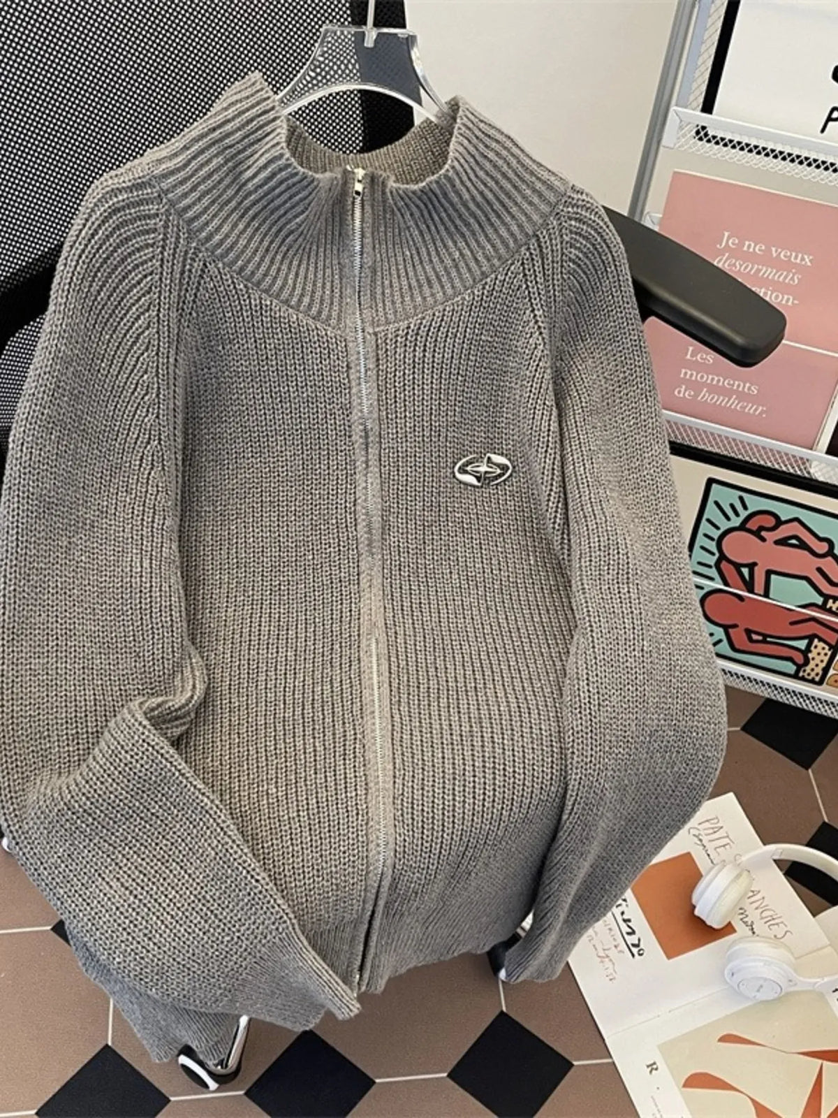 Gray ribbed zip-up cardigan with mock neck and silver emblem detail.