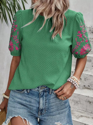 Green embroidered puff sleeve blouse with textured fabric and pink floral sleeve detail.