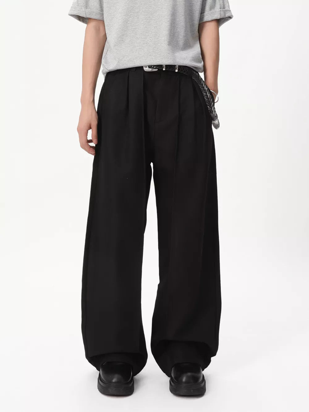 Black relaxed wide-leg pleated trousers with a braided belt and chain detail.